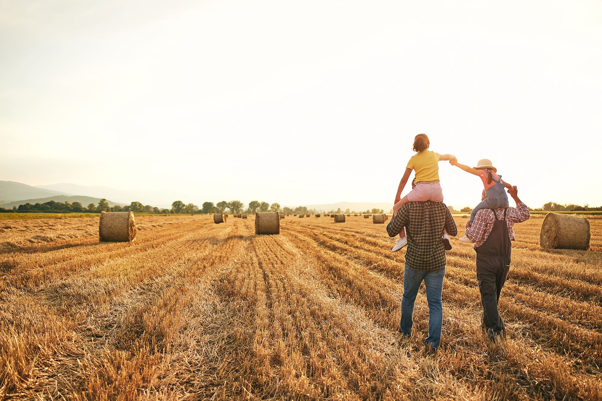 Older Men carrying young girls on shoulders through field